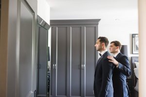 Best man adjusting grooms jacket at home before ceremony.