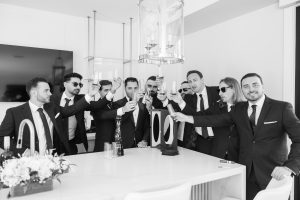 Groom toasting with groomsmen around a kitchen island, raising glasses in celebration