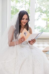 Bride reading a heartfelt card seated in soft window light, veil and lace gown visible