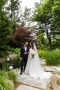 Bride and groom smiling at each other framed by tall trees and greenery