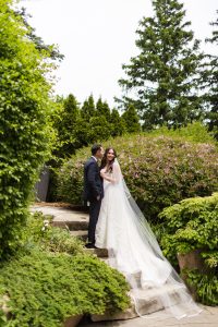 Groom looking at bride, candid laughter framed by flowering shrubs and greenery