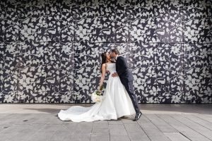 Couple kissing in a graceful dip pose against a large patterned wall mural, bride’s train flowing on the ground in front of them