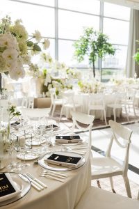 Detailed view of tablescape showing place settings with clear plates, personalized black-and-gold menus, glassware, candles, and white floral arrangements