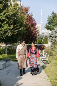 Bride and groom walking hand in hand outside Hotel X Toronto with CN Tower in the background after Tibetan ceremony.