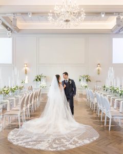 Bride and groom in the Arlington Estate reception space with soft white florals and lace train visible